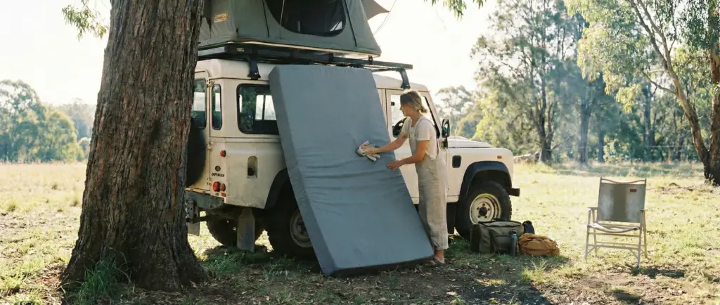 Matelas en mousse de tente de toit sorti pour sécher au soleil contre un arbre.