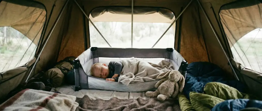 Bébé dormant paisiblement dans un petit lit parapluie sécurisé installé à l'intérieur d'une grande tente de toit familiale.