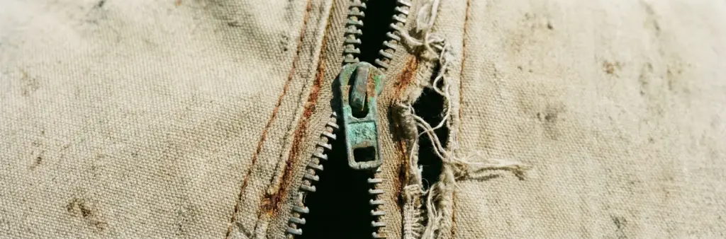 Gros plan sur une fermeture éclair de tente de toit endommagée : curseur rouillé et dents manquantes.