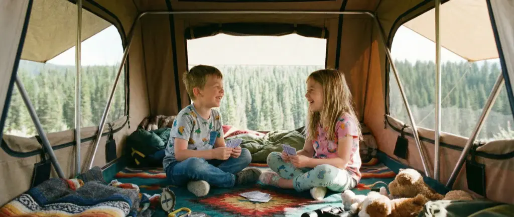 Deux enfants riant et jouant aux cartes à l'intérieur d'une tente de toit spacieuse, considérant l'espace comme une cabane.