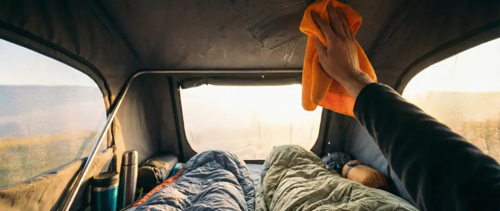 Campeur essuyant la condensation sur les parois intérieures d'une tente de toit avec une serviette microfibre.