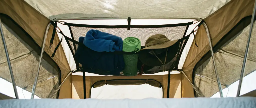 Filet de rangement fixé au plafond d'une tente de toit contenant des vêtements légers et une veste.