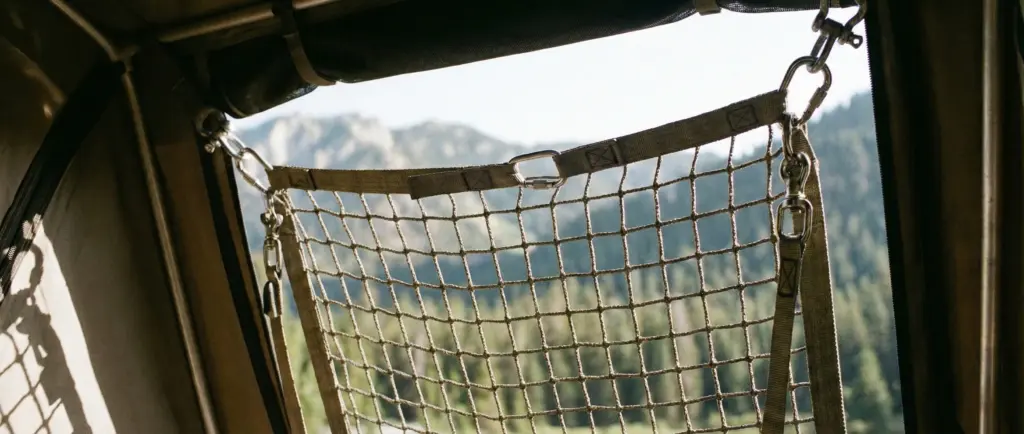 Gros plan sur un filet de sécurité anti-chute installé à l'entrée d'une tente de toit pour protéger l'espace de sommeil.