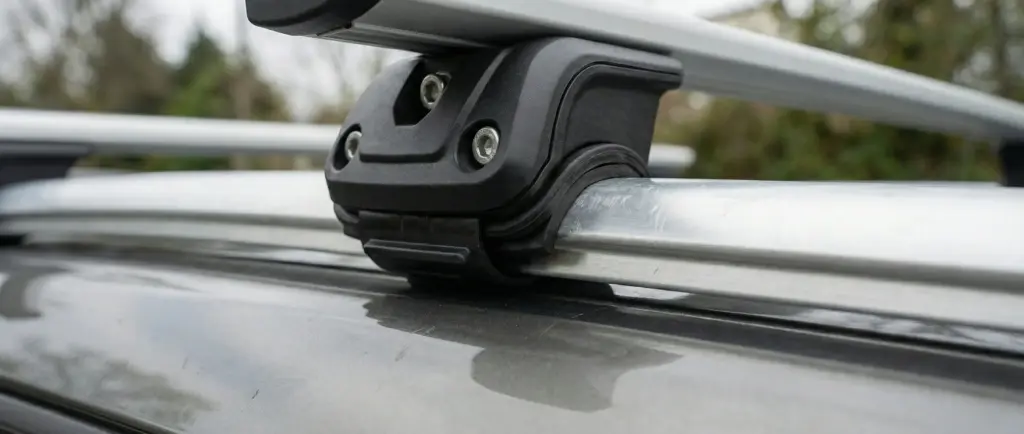 Gros plan détaillé d'un pied de fixation de barre de toit robuste (type Thule) fermement serré sur le rail longitudinal d'une voiture, illustrant la sécurité pour une tente de toit.