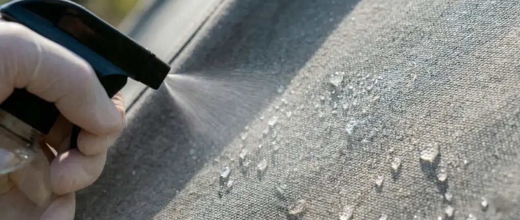 Application d'un spray imperméabilisant sur la toile d'une tente de toit, effet déperlant visible.