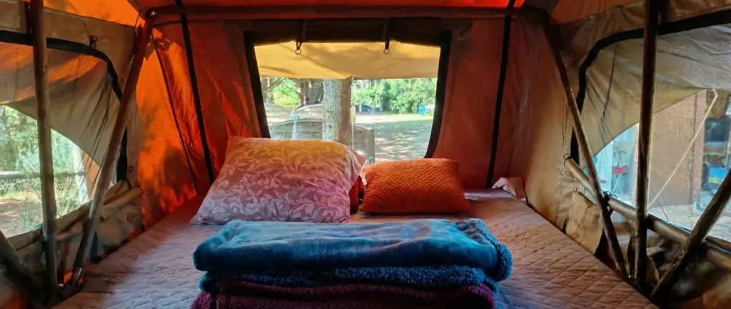 Vue de l'intérieur rangé et spacieux de la tente de toit Swisskings 160, montrant un grand matelas confortable et des couvertures pliées, avec vue sur la nature par l'ouverture.