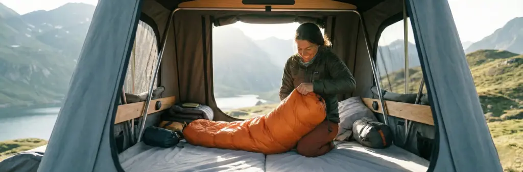 Campeur en train de ranger un sac de couchage dans un sac de compression à l'intérieur d'une tente de toit.