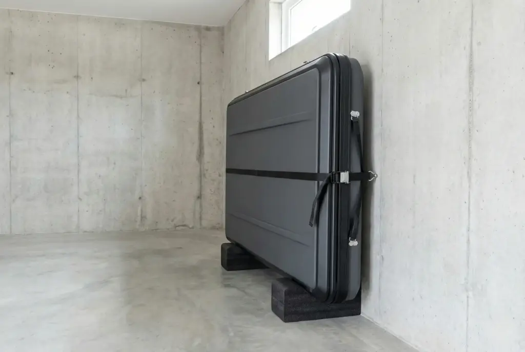 Tente de toit rigide stockée à la verticale contre un mur de garage sur des supports rembourrés.