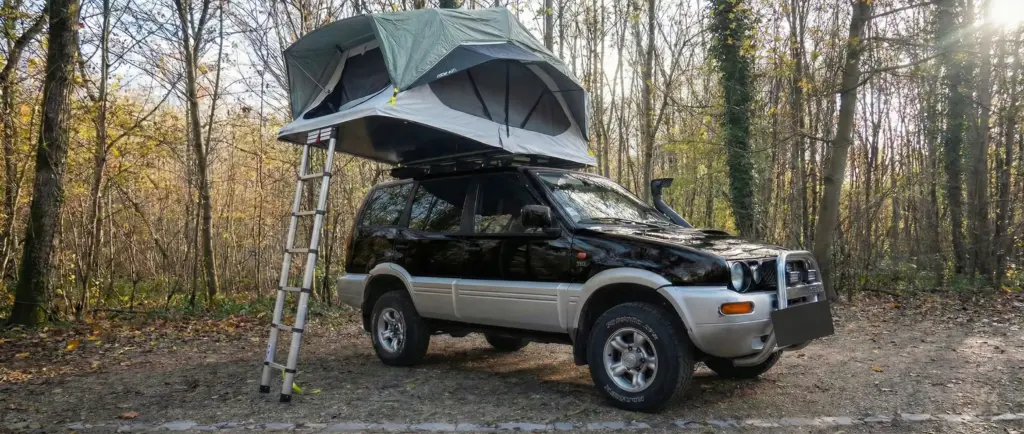 Tente de toit Quechua MH500 de Decathlon dépliée sur un 4x4 noir en pleine forêt.