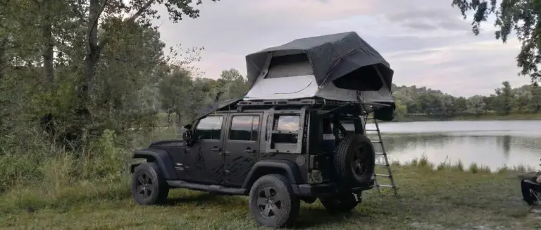 Tente de toit Décathlon Quechua MH500 dépliée sur un Jeep Wrangler noir en bivouac au bord d'un lac.