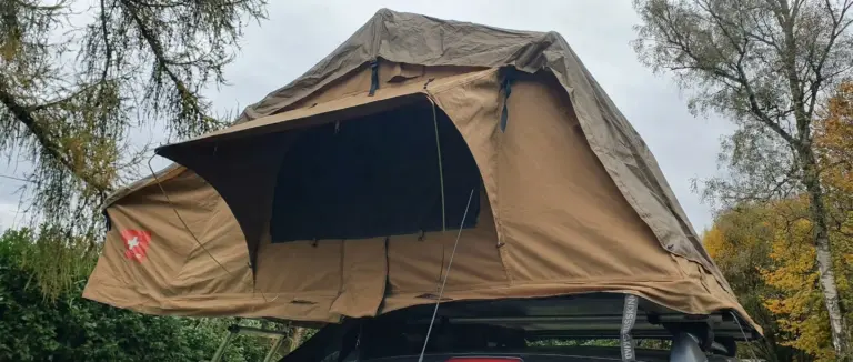 Tente de toit souple SwissKings 140L de couleur beige dépliée et installée sur les barres de toit d'une voiture en extérieur.