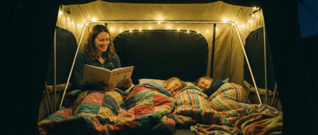 Maman lisant une histoire à deux enfants dans une tente de toit éclairée par une veilleuse douce la nuit.