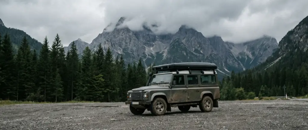 Voiture équipée d'une tente de toit stationnée seule sur un parking de randonnée isolé en montagne